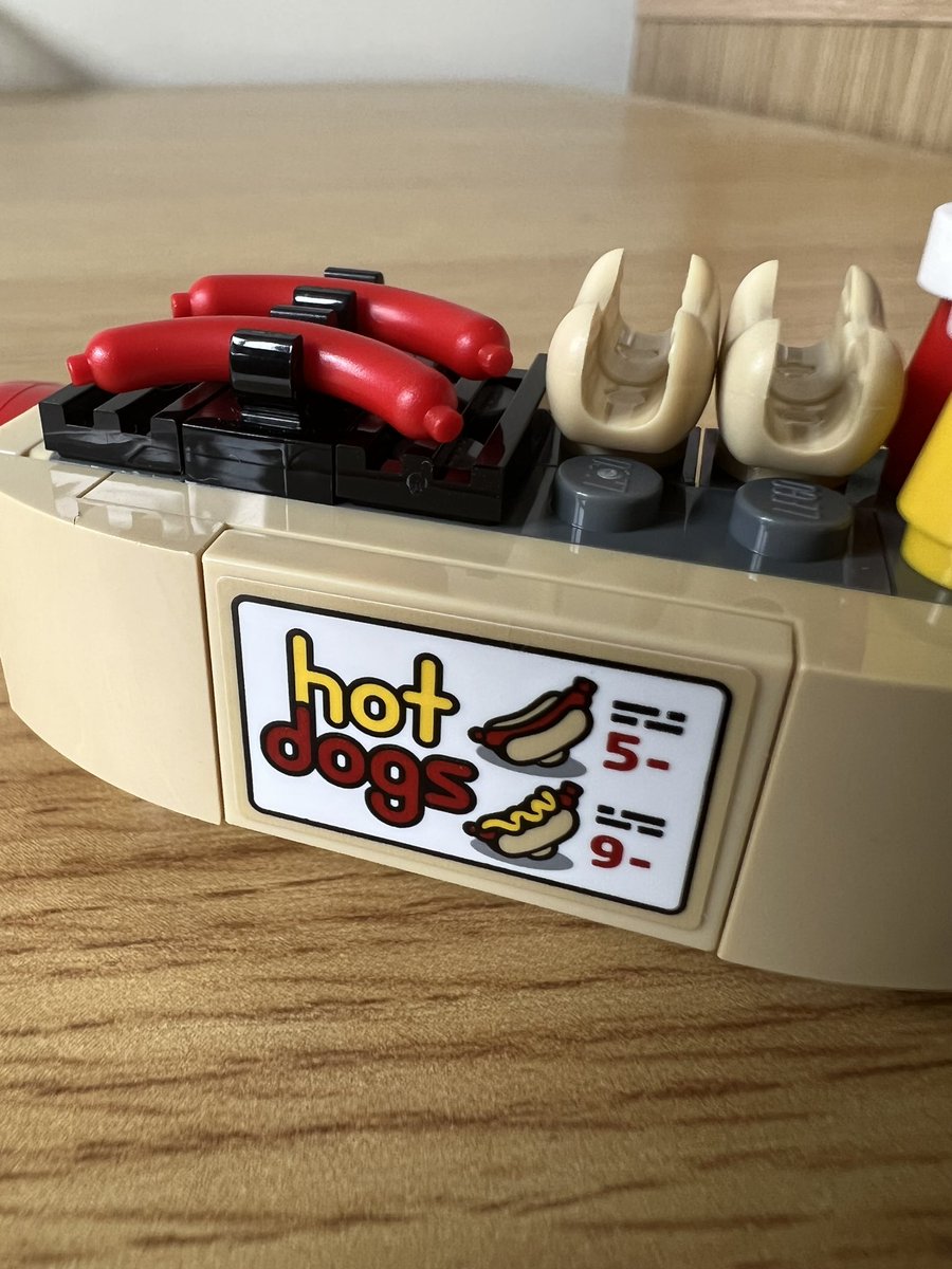 A closeup of the sign on a lego hot dog cart. A plain hot dog is listed as 5, and a hot dog with mustard is 9.