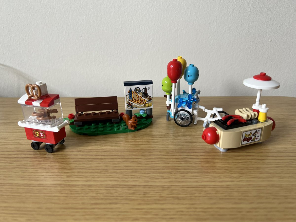 Four small lego models. From left to right there’s a pretzel cart, a bench and amusement park map, a balloon cart, and a hot dog cart shaped like a giant hot dog