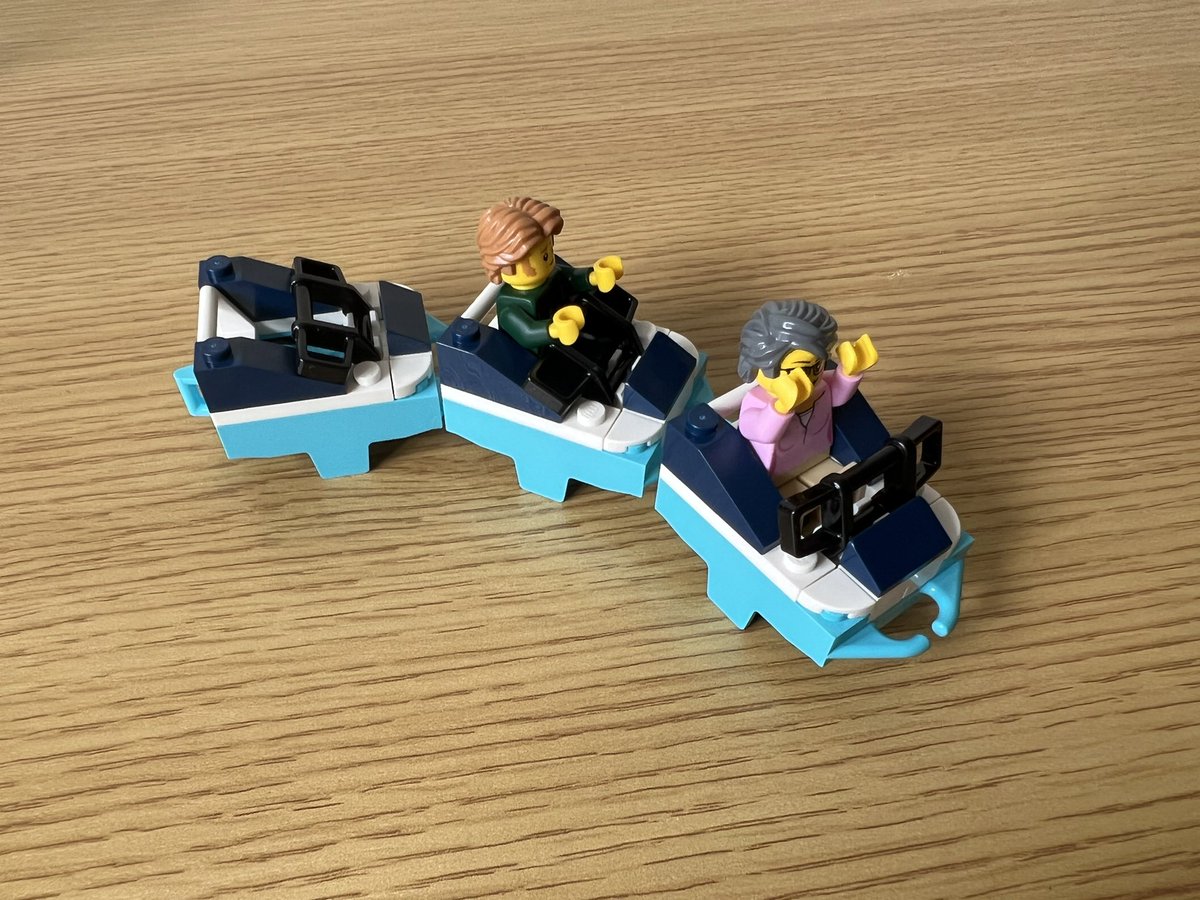 A lego roller coaster train with 3 cars. They are two shades of blue. There are minifigures in two of the cars, one with the lap bar up and one with it down