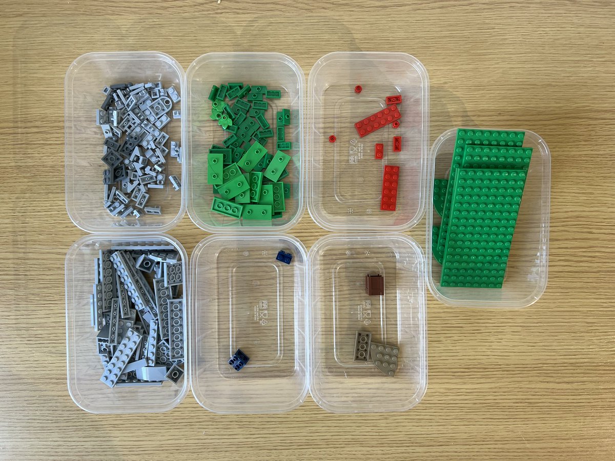 Seven small tubs of lego sorted by colour. The pieces are mostly grey and green, but there are a few red, brown, and blue pieces