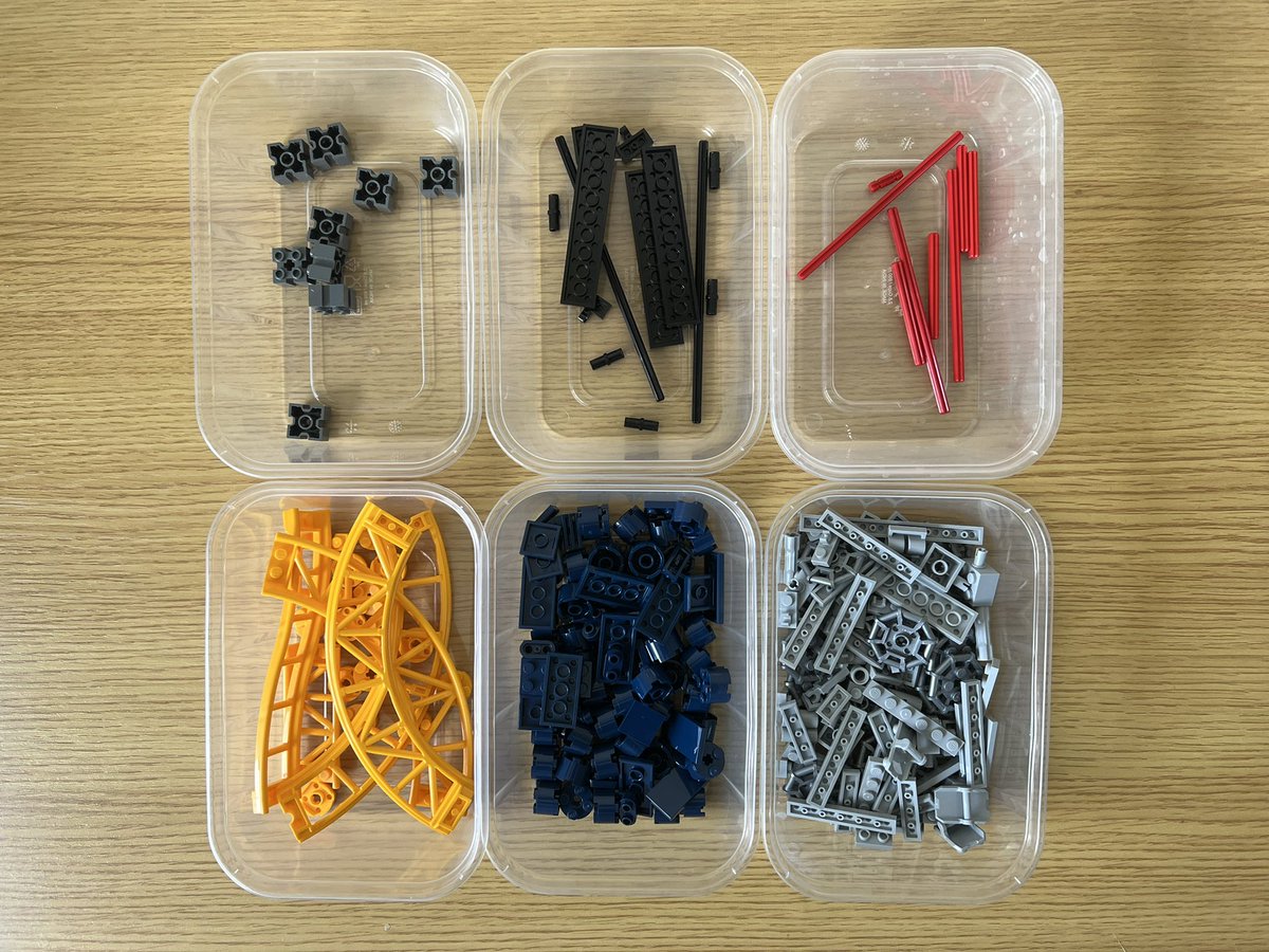 Six tubs of lego sorted by colour. There are grey, black, red, blue, and yellow pieces. The tub with the yellow pieces contains some roller coaster track.