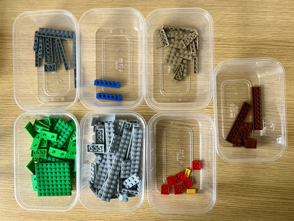 Seven plastic tubs of lego sorted by colour. There’s a lot of green and grey, and a few red and blue pieces.