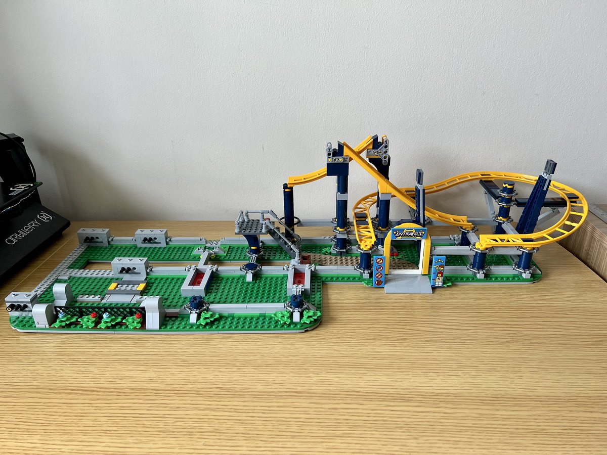 A partially built lego roller coaster. The left side is mostly empty and on the right side is a few pieces of disconnected track as well as an entrance archway.