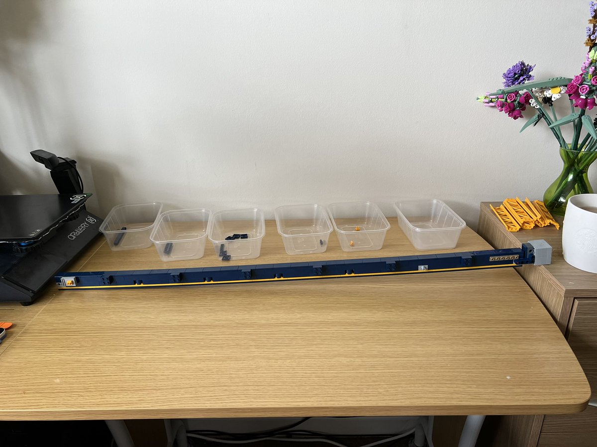 A lego structure that’s so long it doesn’t fit on the desk and is resting on a filing cabinet next to the desk.