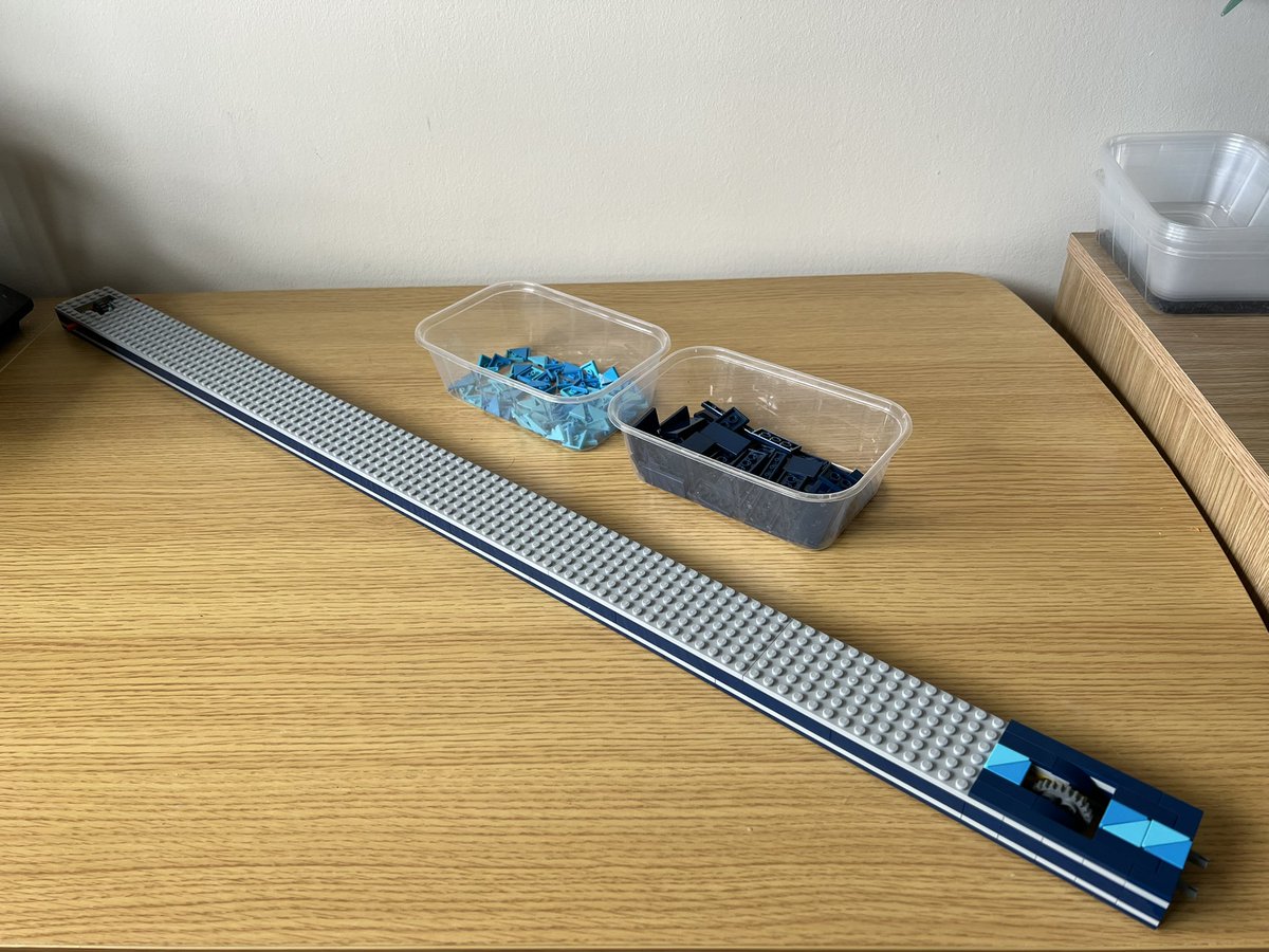 A very long lego structure that’s mostly grey on top but the very end has a pattern of tiles in different shades of blue forming diagonal stripes.