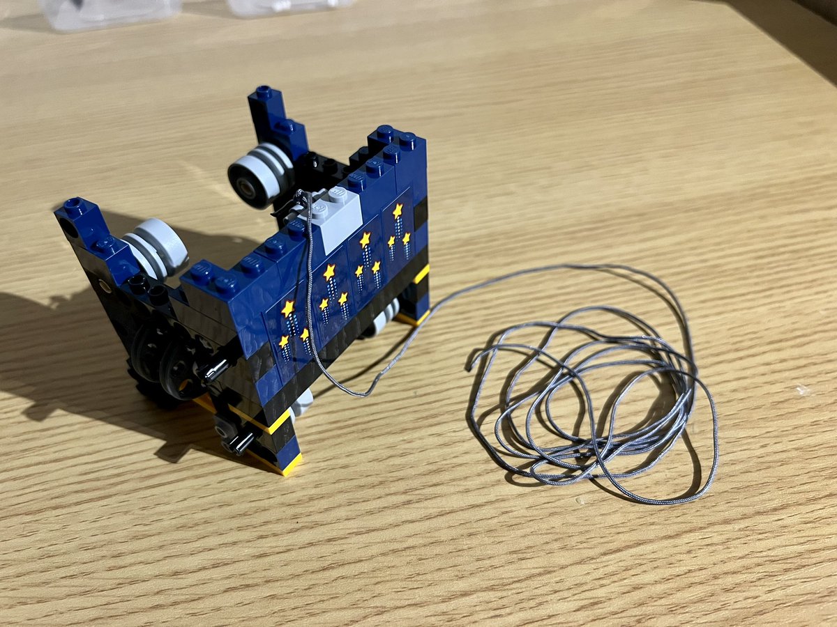 The back of a lego structure that has a shooting star design. There’s a long piece of string attached to the top and coiled up on the desk.