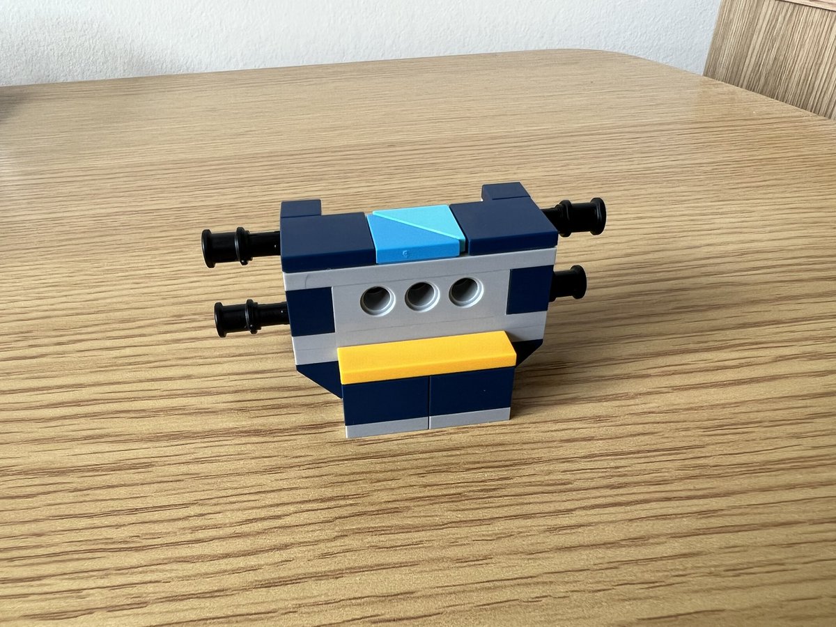 A lego structure with holes in the front and black legs sticking out the side. There’s a small yellow lip below the holes, and triangles in two shades of blue on the top.