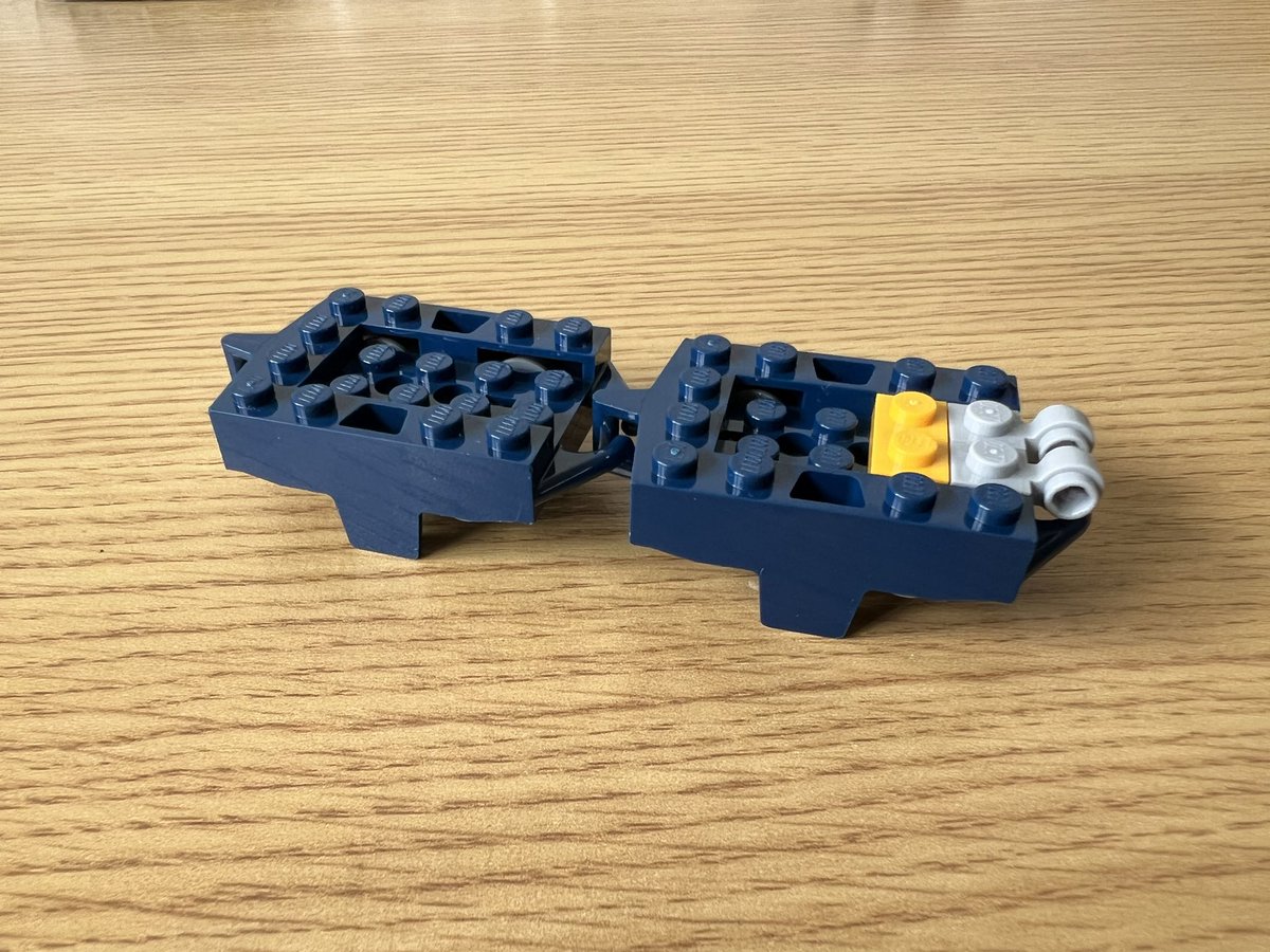 Two dark blue lego roller coaster cars attached together.