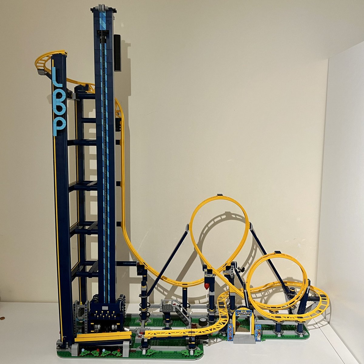 A lego roller coaster with blue supports and yellow track. It has a tall tower on the left leading into a vertical drop and two loops before curving back round to the beginning. There’s a chain lift going up the tower. A tiny segment of track is missing between the end of the track and the lift.