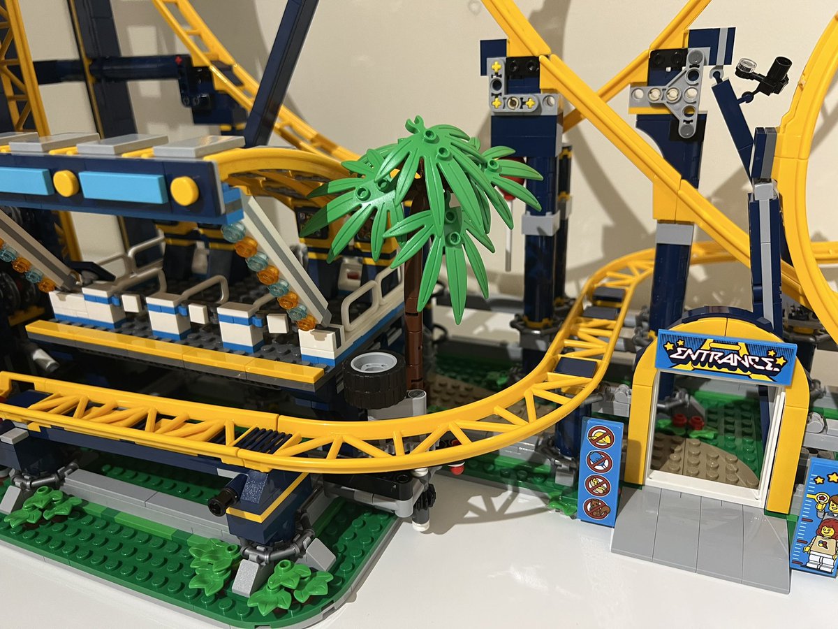 A lego palm tree in between the station platform and entrance archway of a roller coaster.