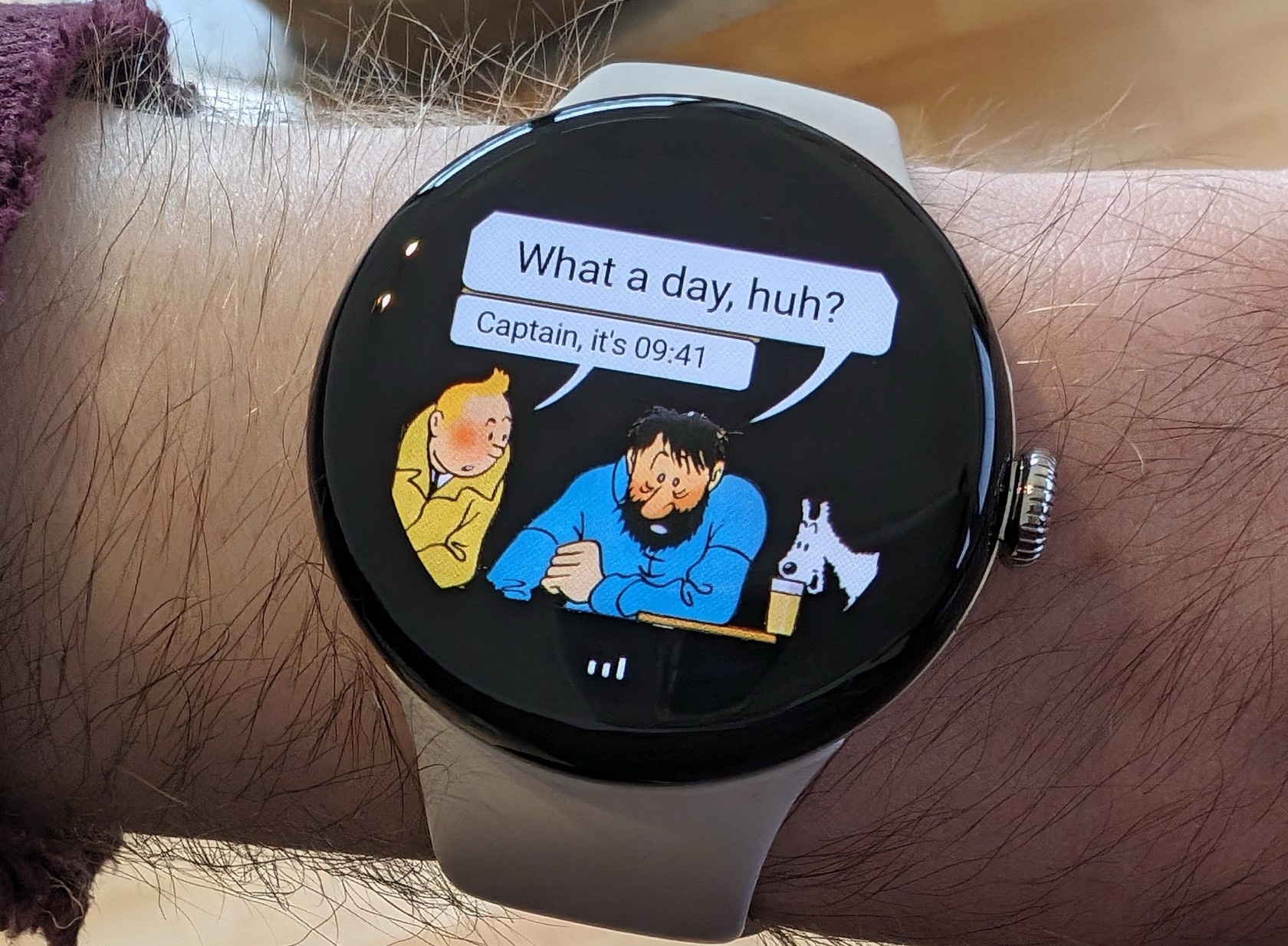 A Pixel Watch with a watch face showing an illustration of Tintin and Captain Haddock sitting at a bar. Captain Haddock is saying "What a day, huh?", and Tintin is replying "Captain, it's 09:41".