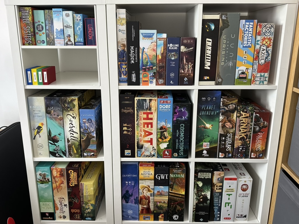A white shelving unit divided into square sections, each containing around 4 board games.